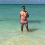 From Beach Babe to Boardroom Boss ! Shirtless Nigel de Csernatony standing in the ocean in Mexico, wearing bright pink swim trunks.