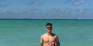 From Beach Babe to Boardroom Boss ! Shirtless Nigel de Csernatony standing in the ocean in Mexico, wearing bright pink swim trunks.